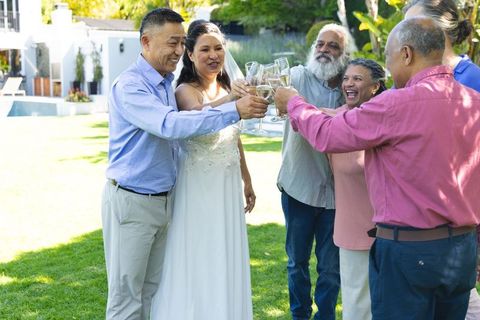 Bride leading toast with guests raising champagne glasses at backyard poolside wedding