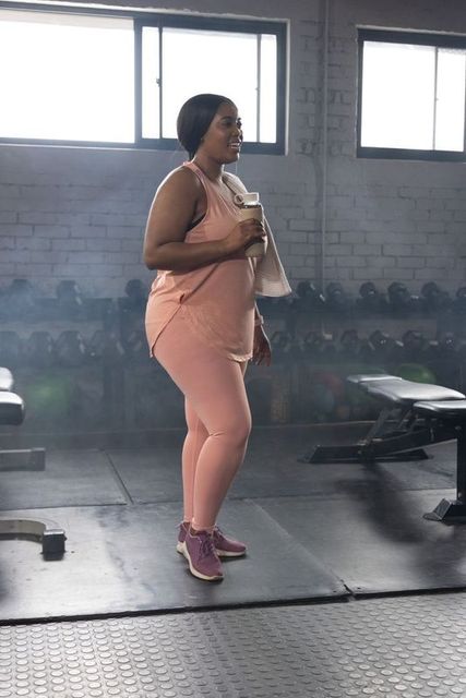 African american woman exercising in gym wearing pink activewear holding water bottle and towel