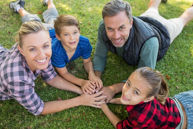 Happy family lying and putting their hands together in park - Download Free Stock Photos Pikwizard.com