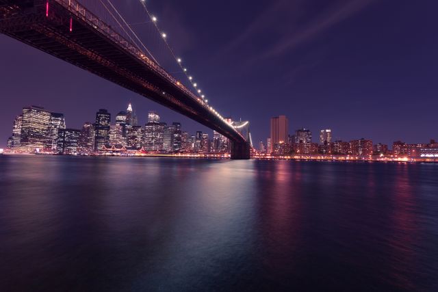 Photo depicts majestic Brooklyn Bridge and stunning New York City skyline illuminated at night. Ideal for travel blogs, city guides, wallpaper, or any project showcasing urban beauty and iconic landmarks of NYC.