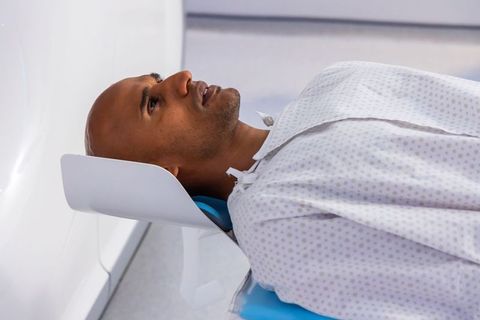 African american man lying in mri gantry wearing hospital gown before diagnostic scan