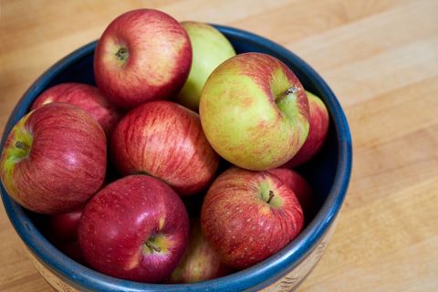 Fresh red and green apples in blue ceramic bowl on wooden countertop healthy fruit
