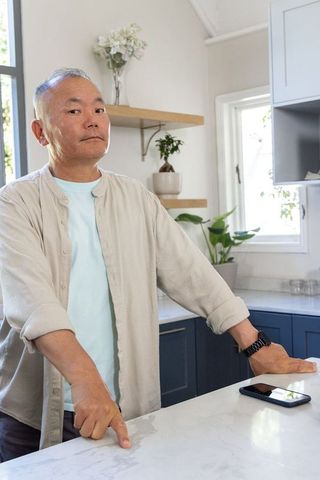 Asian mature man leaning and pointing at marble countertop in modern minimalist kitchen