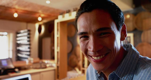 Man smiling warmly in a rustic wine cellar with wooden barrels, creating a cozy and inviting atmosphere. This image can be used for hospitality, winery promotions, casual lifestyle blogs, or advertisements promoting social gatherings and cheerful settings.