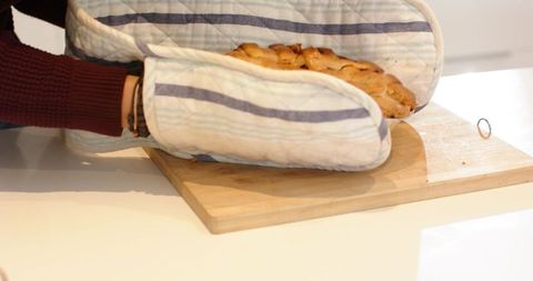 Removing braided loaf with striped oven mitts on wooden cutting board in bright minimal kitchen