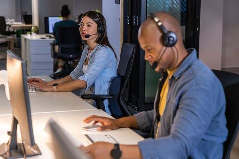 Diverse call center team collaborating at desks with headsets and computers in modern office