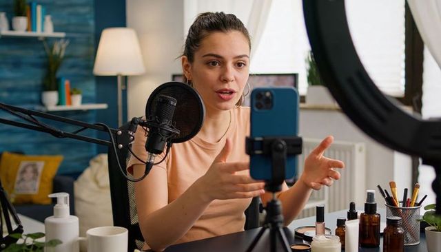 Beauty creator recording skincare tutorial using smartphone, microphone and ring light