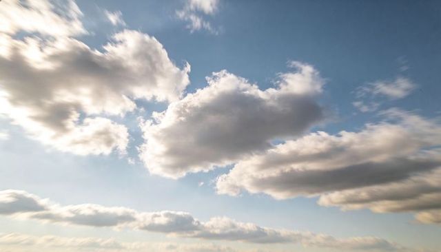 Sunlit cumulus cloud drifting across expansive blue sky with layered stratocumulus bands