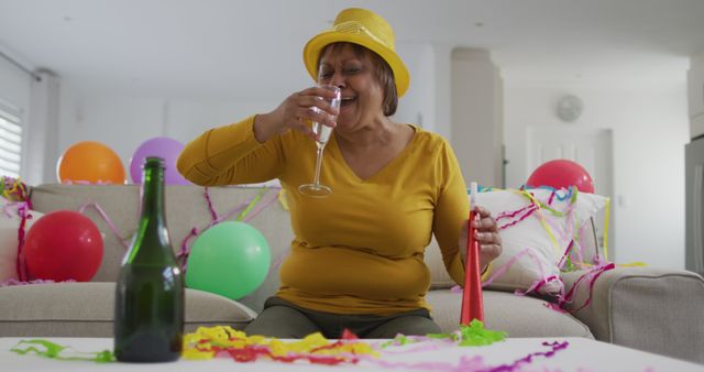 African american senior woman celebrating with champagne and party blower, on new year's image call. active, youthful retirement lifestyle, celebrating at home with communication technology.