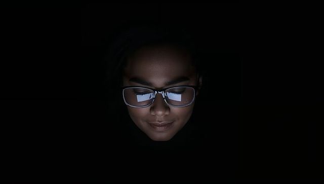 Soft-lit face with rectangular glasses glowing from tablet screen in dark moody portrait
