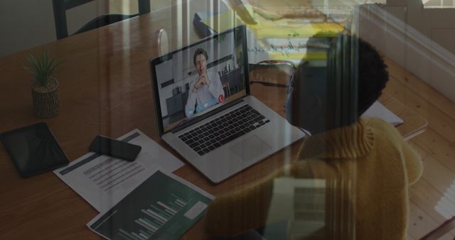 Depicts an individual having a business meeting from a home office through video call software on a laptop. Papers with charts and smartphone are on the table, signifying a productive work environment. Could be used for articles or content related to remote work, digital communication, video conferencing, and modern work trends.