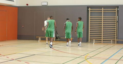 Diverse male basketball team walking into gym warming up for practice before game