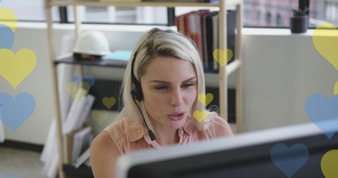 Businesswoman with headset overlaid with hearts supporting ukraine