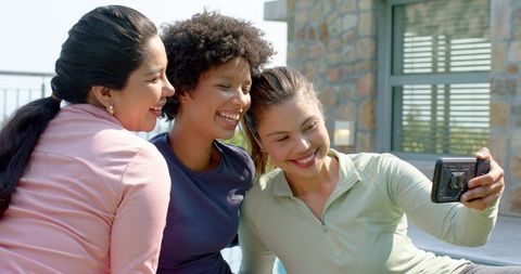 Diverse women taking selfie by pool, laughing and bonding on sunlit patio