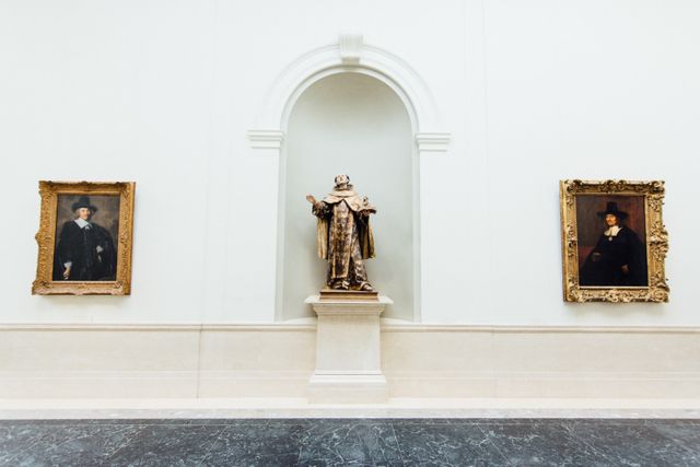 This stock photo can be used to represent the elegance and cultural richness of historical art galleries and museums. The image showcases classical portraits and a central sculpture in a well-lit, sophisticated setting, ideal for articles about art history, museum exhibitions, culture, and interior designing of art spaces.