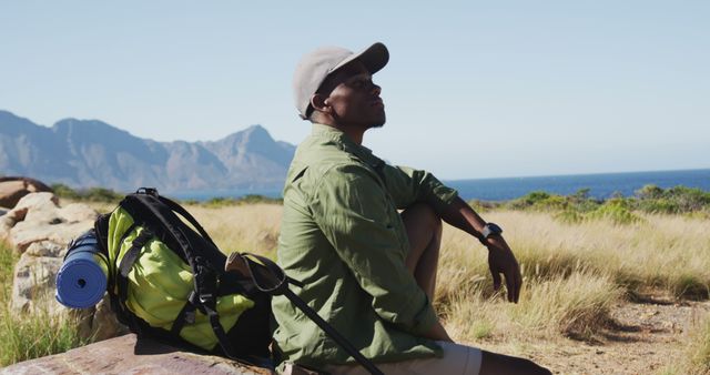 African american man hiking in countryside by the coast taking a rest sitting on a rock. fitness training and healthy outdoor lifestyle.