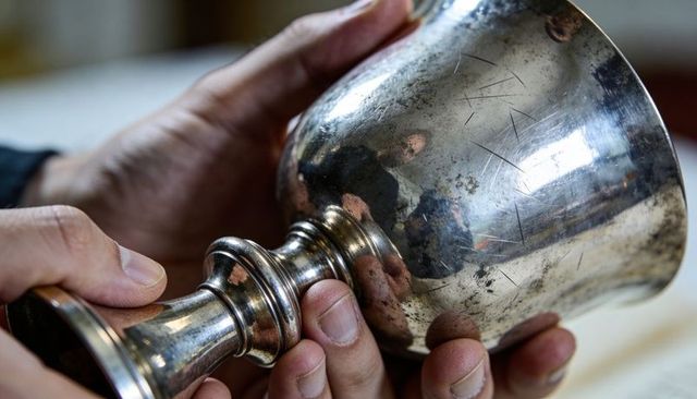 Holding inspecting tarnished silver goblet chalice closeup showing patina scratches