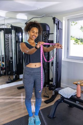 Smiling Woman Holding Measuring Tape in Home Gym, Motivated Fitness Journey