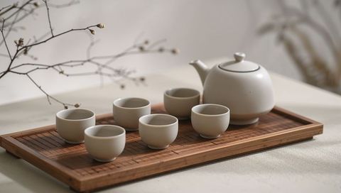Displaying white ceramic teapot and six teacups on bamboo tray with twig accent