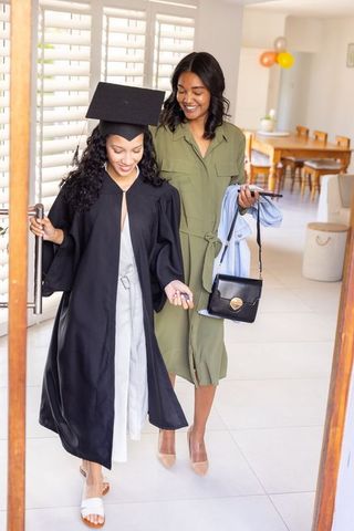 Diverse sisters celebrating graduation at home entering with cap, gown and keys