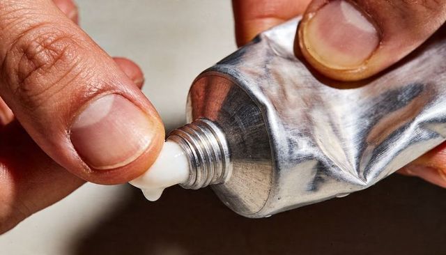 Squeezing aluminum tube dispensing white cream close-up of adult hands and fingertip