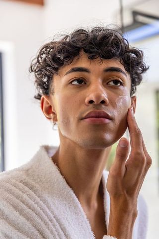 Man in Bathrobe Applying Skincare Cream in Minimalist Bathroom