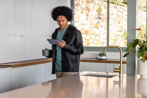African american man using tablet in modern kitchen holding mug at glossy island