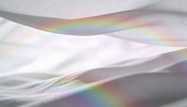 White sheer fabric folding diagonally, revealing prismatic rainbow light streaks, minimalist