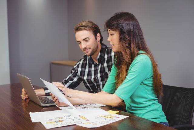 This image shows a male and female designer working together in an office conference room. They are discussing a project with various design materials spread on the table, suggesting a creative and productive work environment. Ideal for use in articles about teamwork, creative industries, project management, and professional work settings.
