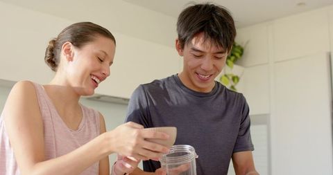 Couple preparing healthy fruit smoothie in bright modern kitchen while smiling together