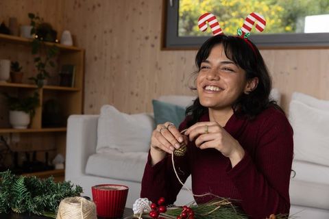 Hispanic woman crafting pinecone wearing antler headband in festive home