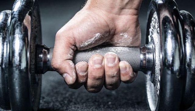 Chalk-dusted hand gripping knurled dumbbell handle closeup, gritty high-contrast gym texture