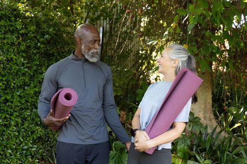 Mature african american man and woman holding yoga mats smiling together in garden