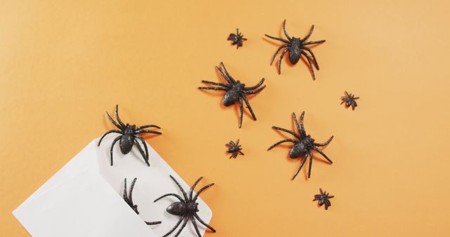 Multiple spider toys coming out of a envelope against orange background. halloween festivity and celebration concept