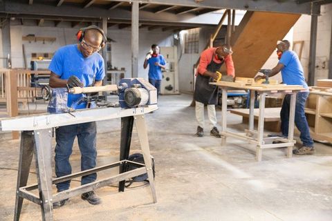 African american craftsmen shaping wood on lathe in busy workshop with protective gear