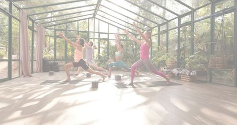 Sunlit Group Yoga Practicing High Lunge in Glass Conservatory Surrounded by Greenery