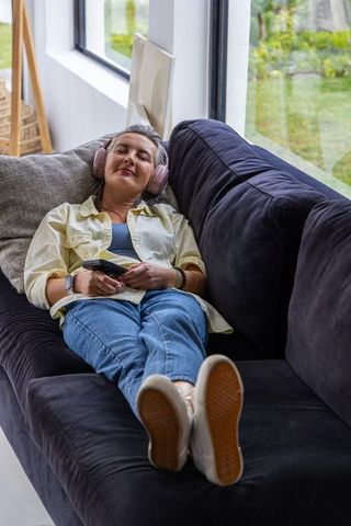 Middle-aged woman relaxing on sofa listening to music with headphones and smartphone