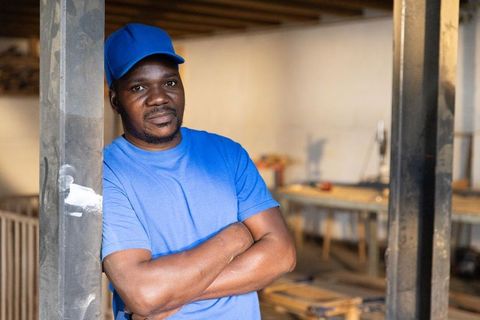 African american worker leaning on metal beam crossing arms in workshop