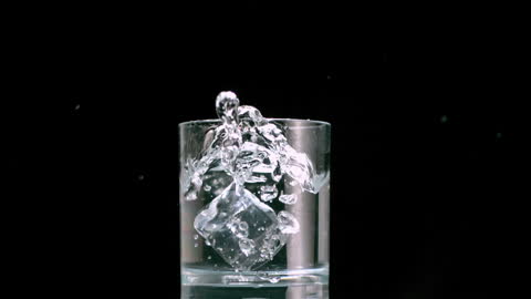 Splashing Water and Ice Cube in Glass on Black Background