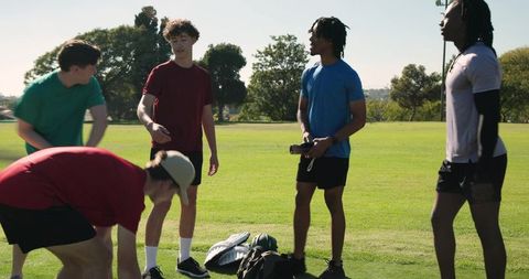 Multiracial teen baseball team gathering on sunny grass field preparing for practice