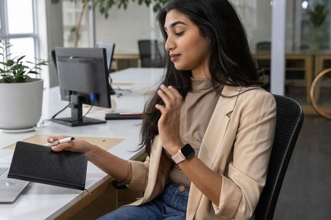 Late-20s indian professional woman holding notebook and working at modern open-plan desk