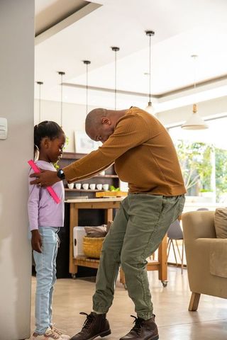 Measuring daughter height against wall in sunlit open-plan kitchen