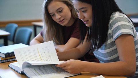 High School Students Studying Together Reviewing Math Textbook Worksheets and Notes in Classroom