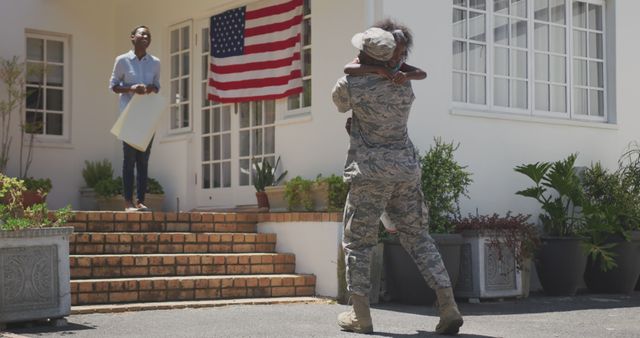 Happy african american male soldier and his family embracing and greeting outside the house. Military, patriotism, family, and togetherness.