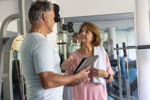Senior fitness coaching male trainer guiding mature woman through personalized gym workout