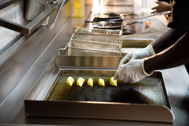 Side view close up of an African American male chef working in a restaurant kitchen, preparing dumplings to be fried, lying them down in a row, next to a fryer