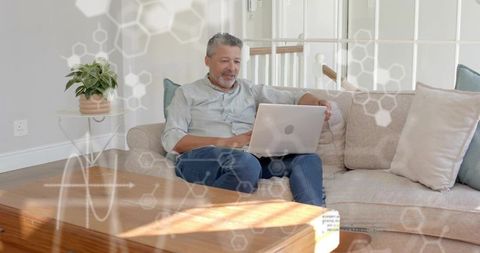 Mature man using laptop on sofa in sunny living room with molecular overlay for remote work