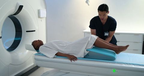 Radiology technician positioning patient on ct scanner using blue wedge for pelvic imaging