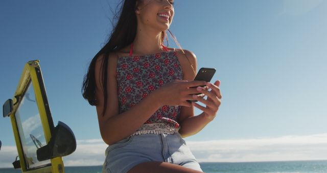 Happy caucasian woman sitting on beach buggy by the sea talking on smartphone. beach stop off on summer holiday road trip.