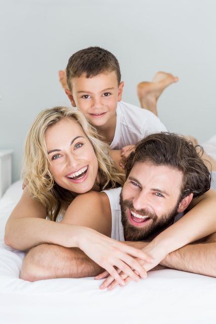 This image shows a happy family consisting of parents and their son lying on a bed and smiling. It can be used for promoting family-oriented products, lifestyle blogs, parenting articles, or advertisements focusing on family bonding and happiness.